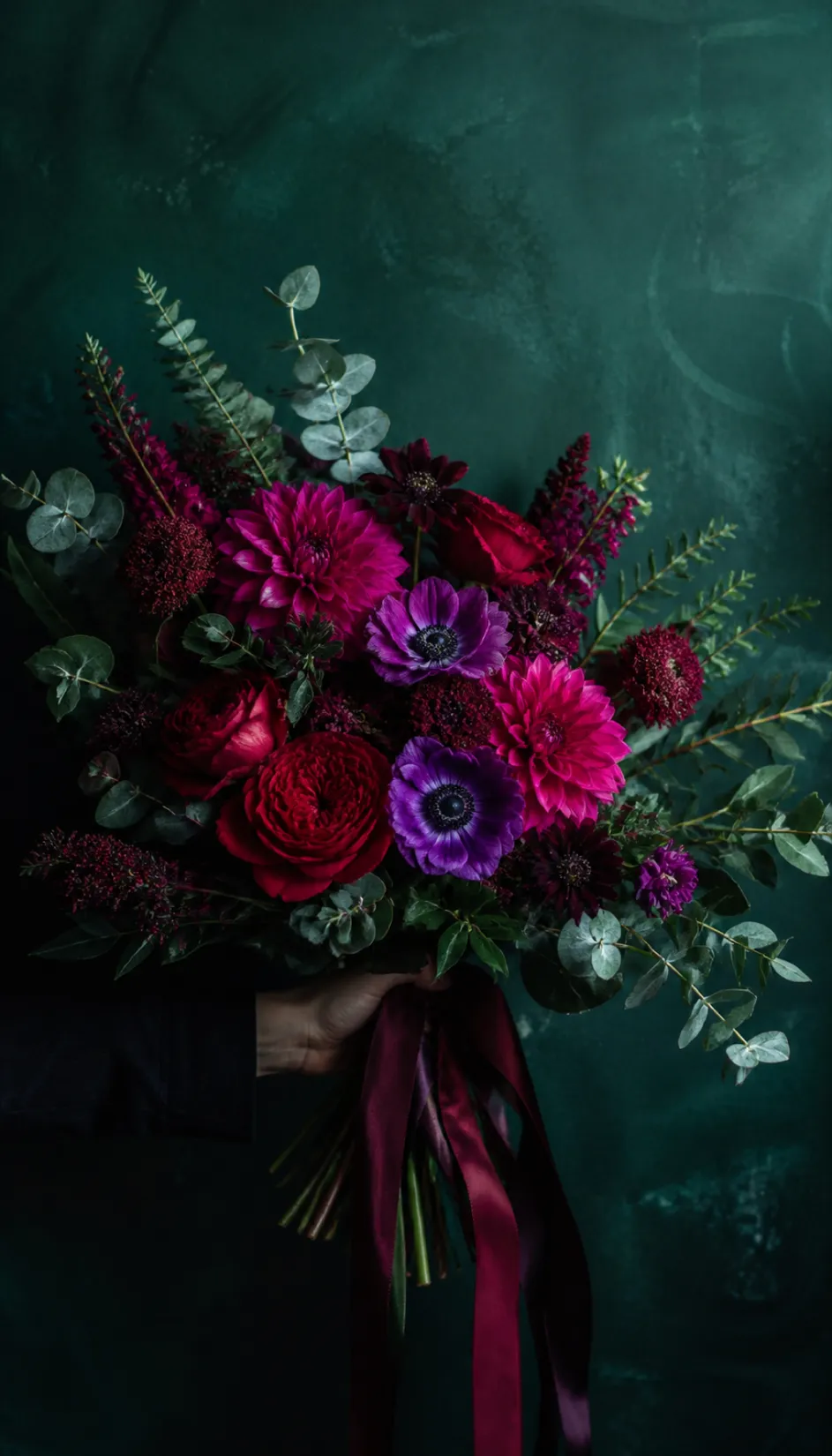 Hand-tied bridal bouquet of fuchsia dahlias, deep red garden roses and violet anemones with trailing burgundy ribbons